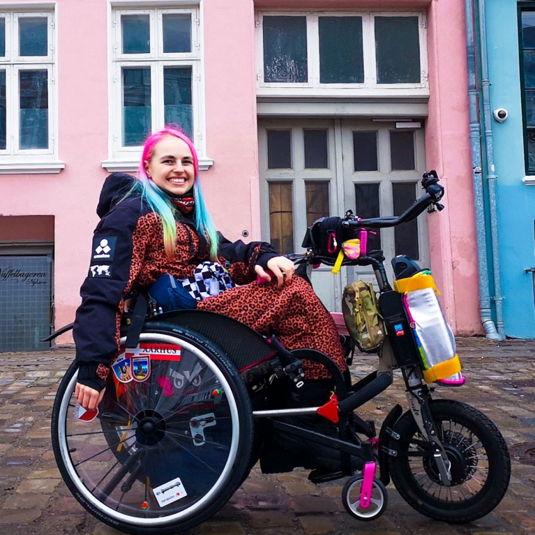 kris-travels-in-a-wheelchair-in-front-of-colorful-houses
