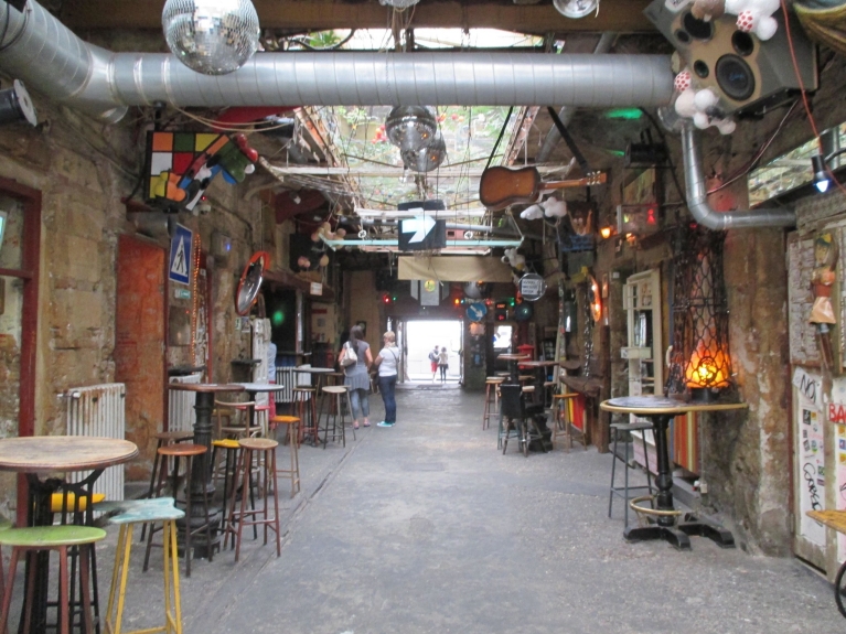 Image of ruin pub in Budapest with tables and stools, and decorations hanging from the ceiling.