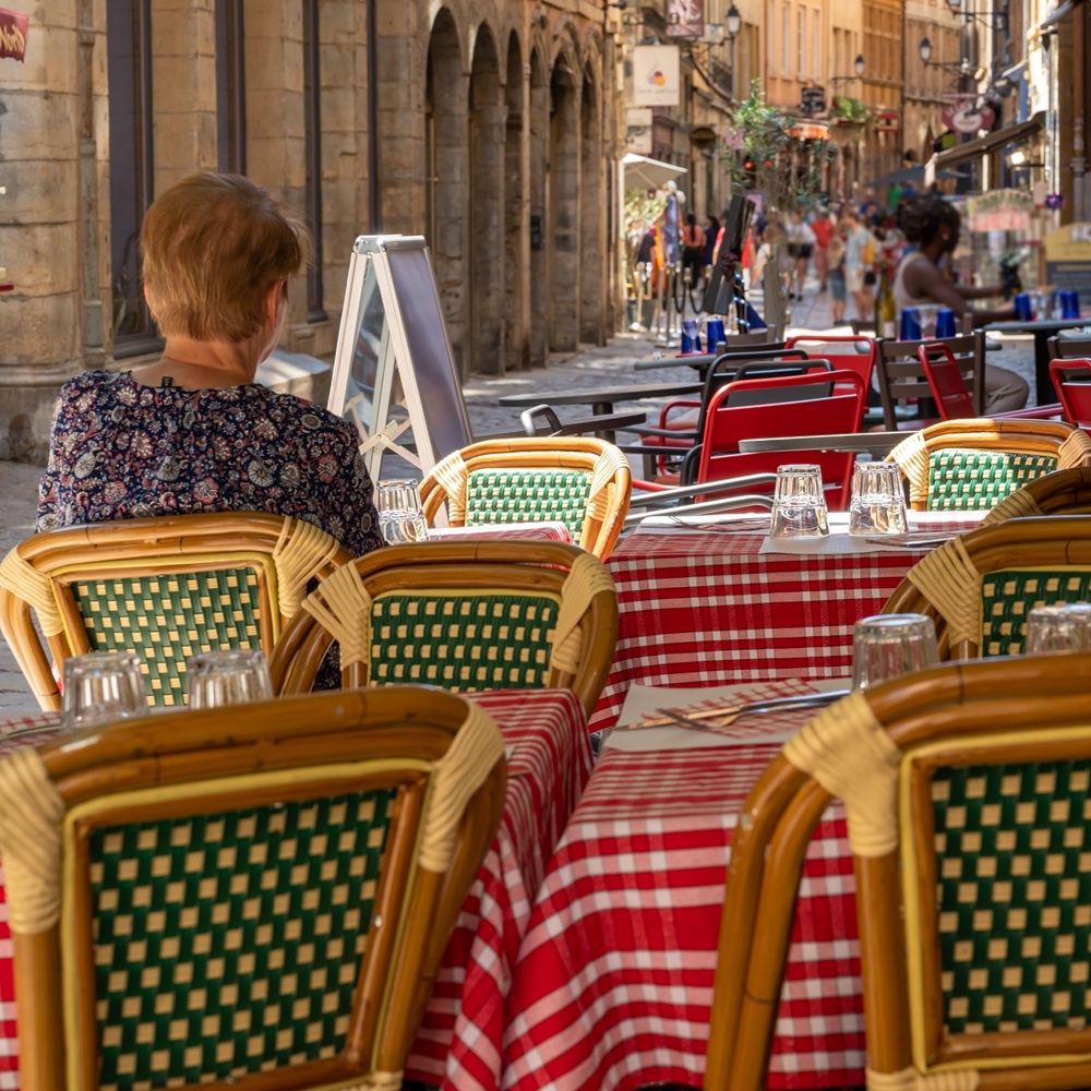 A woman sitting at a small outdoor table at a restaurant in Lyon