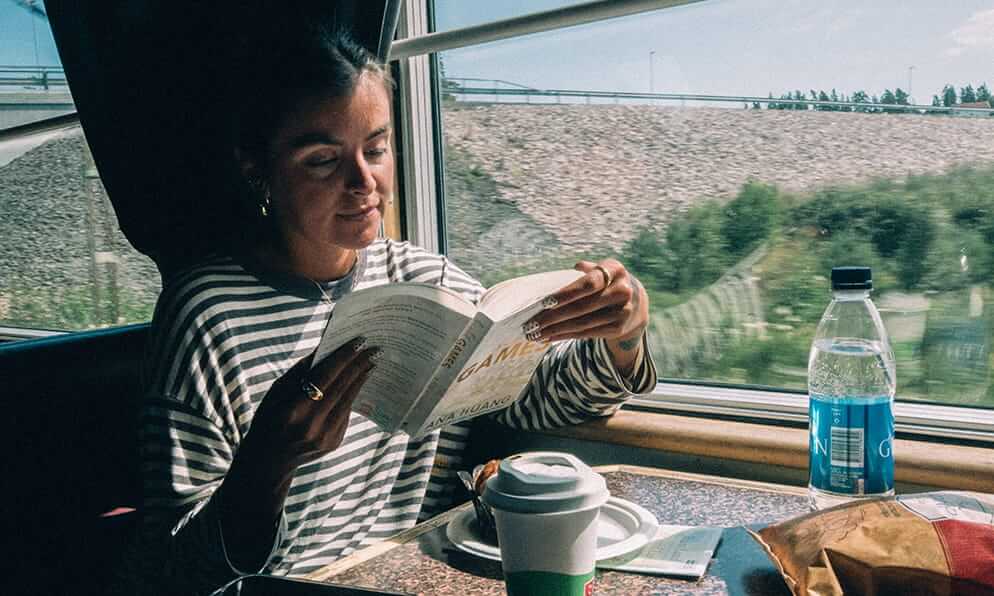 A woman reads a book in a window seat on a train