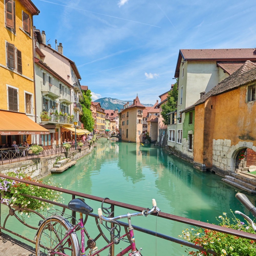 Una vista de uno de los canales azul-verde de Annecy, con edificios amarillos y blancos a cada lado del agua