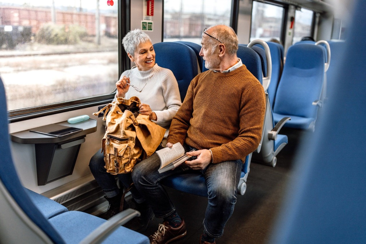 Un couple d'âge mûr voyageant en train, assis l'un à côté de l'autre, lisant un livre et profitant du trajet.