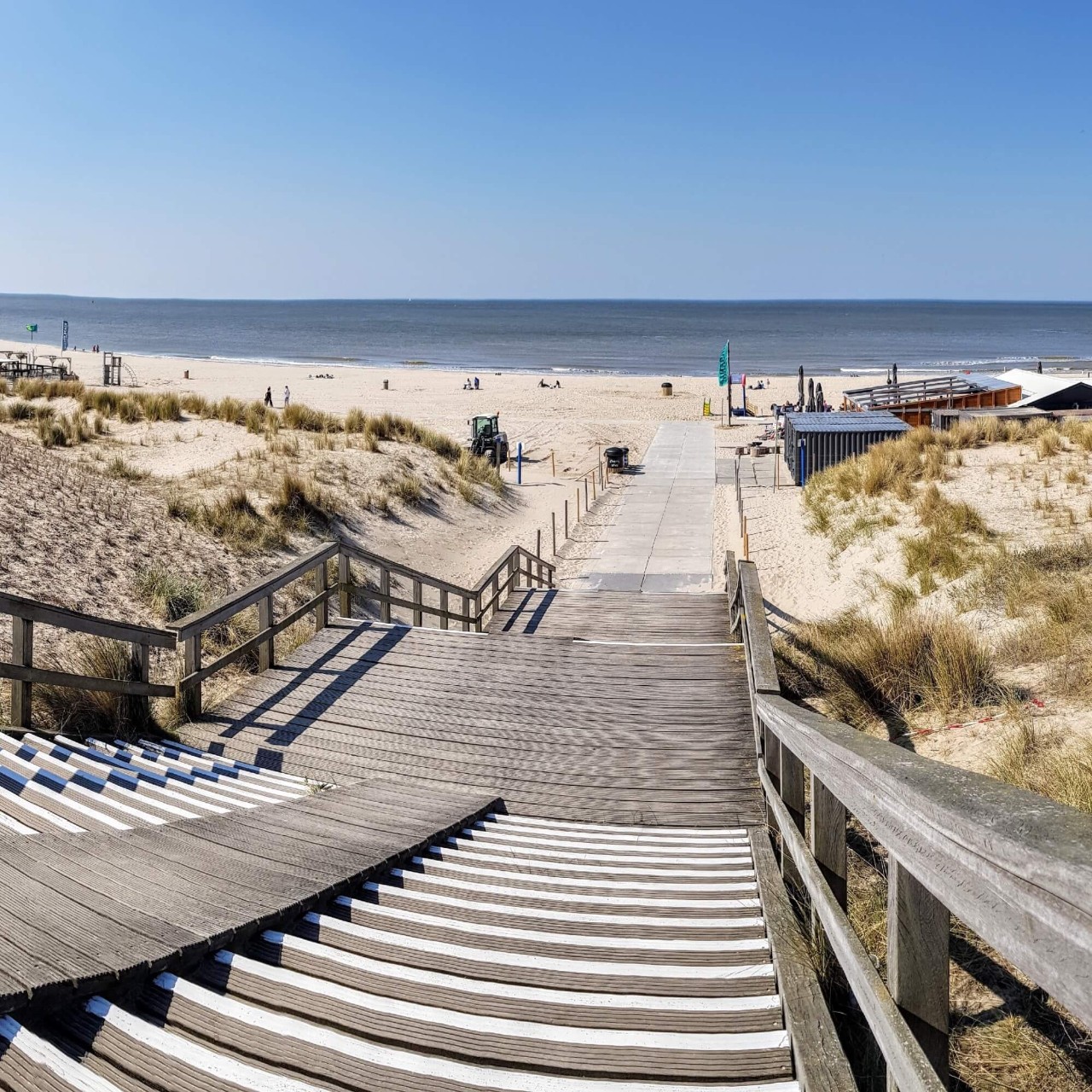 Des marches en bois descendant vers une plage de sable blanc avec l’océan en arrière-plan.