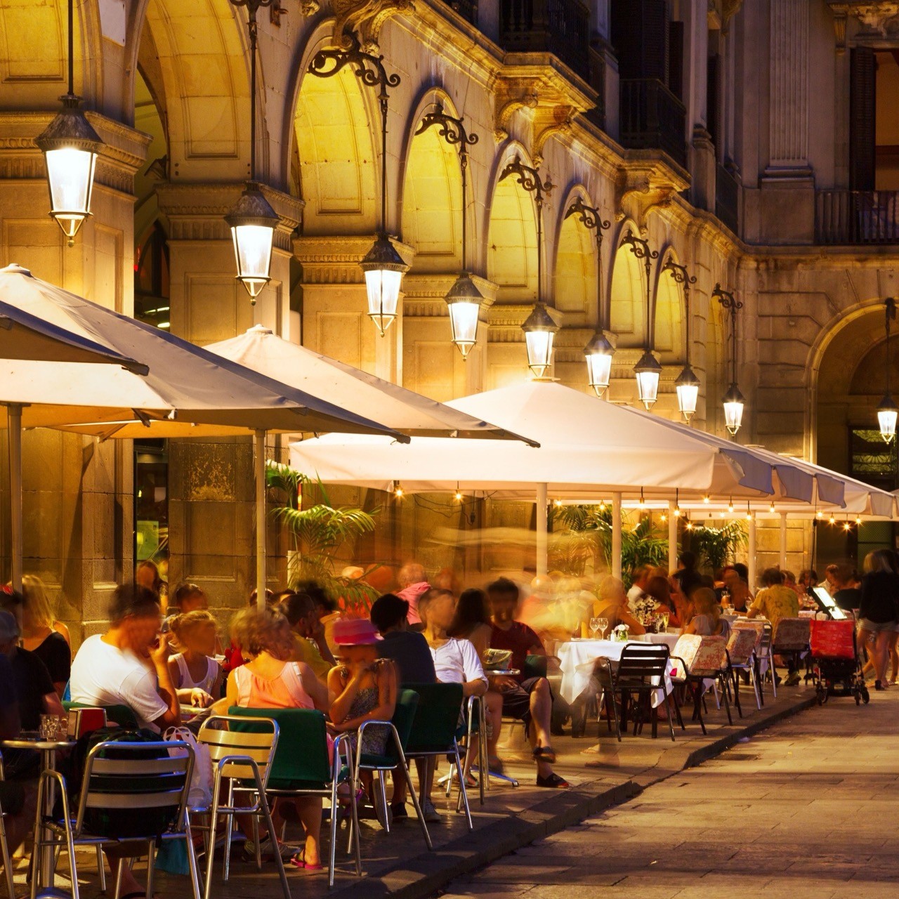 Persone sedute ai tavoli all'aperto a Barcellona, di notte, sotto le luci della piazza