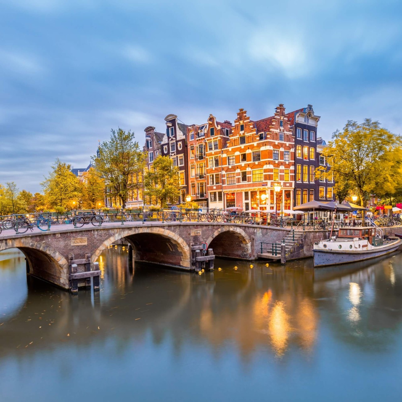 Een blauwe gracht in Amsterdam, overspannen door een brug, met hoge, ouderwetse huizen op de achtergrond