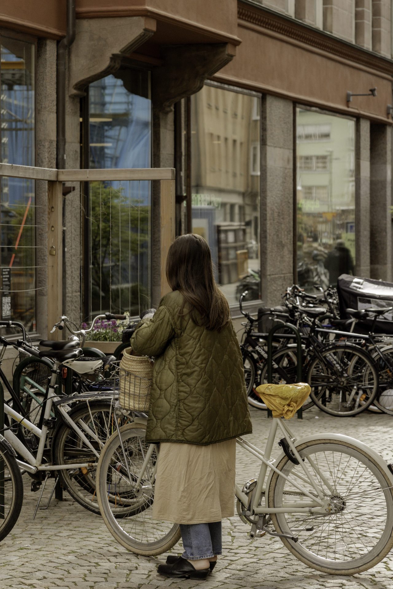 Uma mulher de costas para a câmera, segurando uma bicicleta em uma rua em Malmo, Suécia