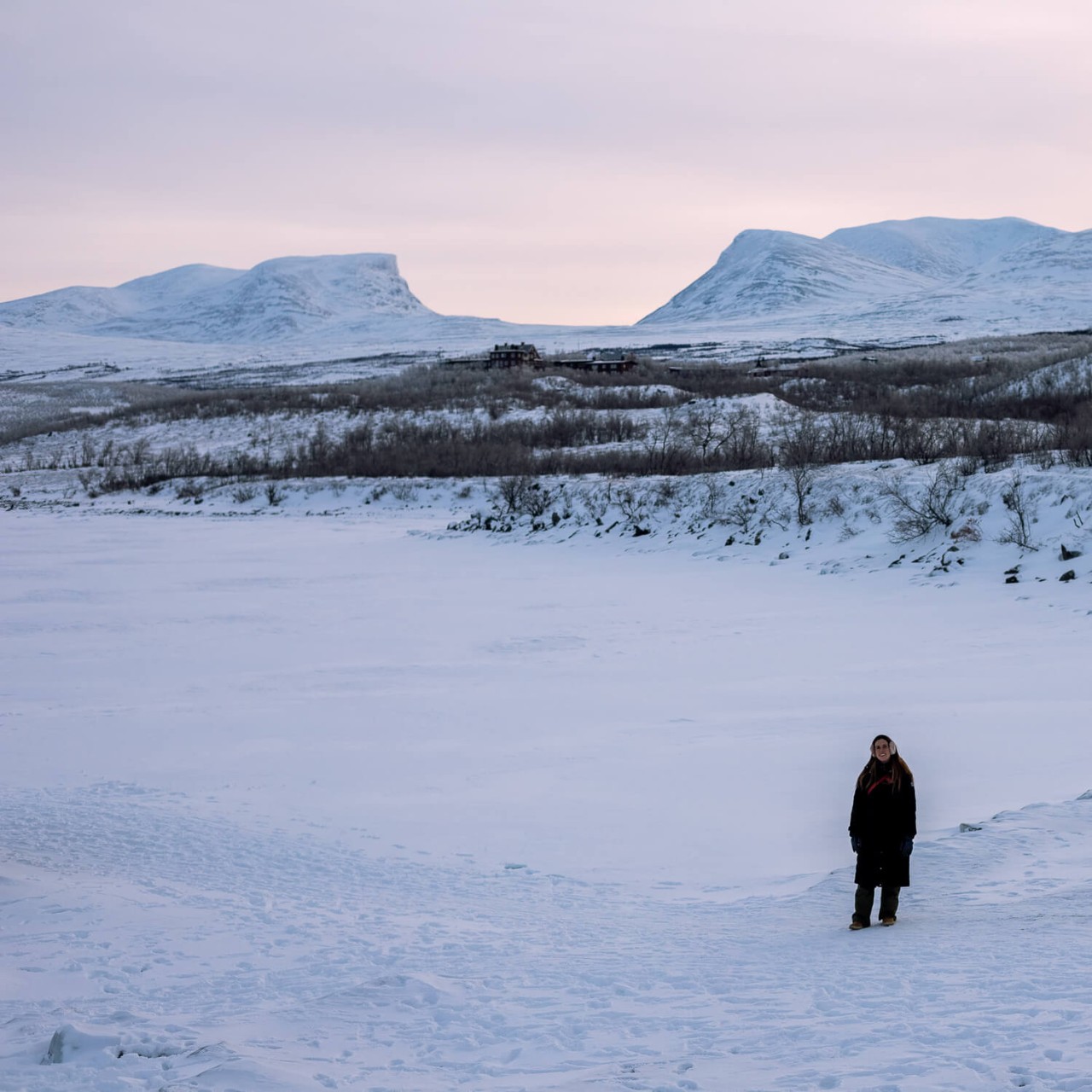 Uma pessoa em pé nas margens de um lago congelado em Abisko, Suécia