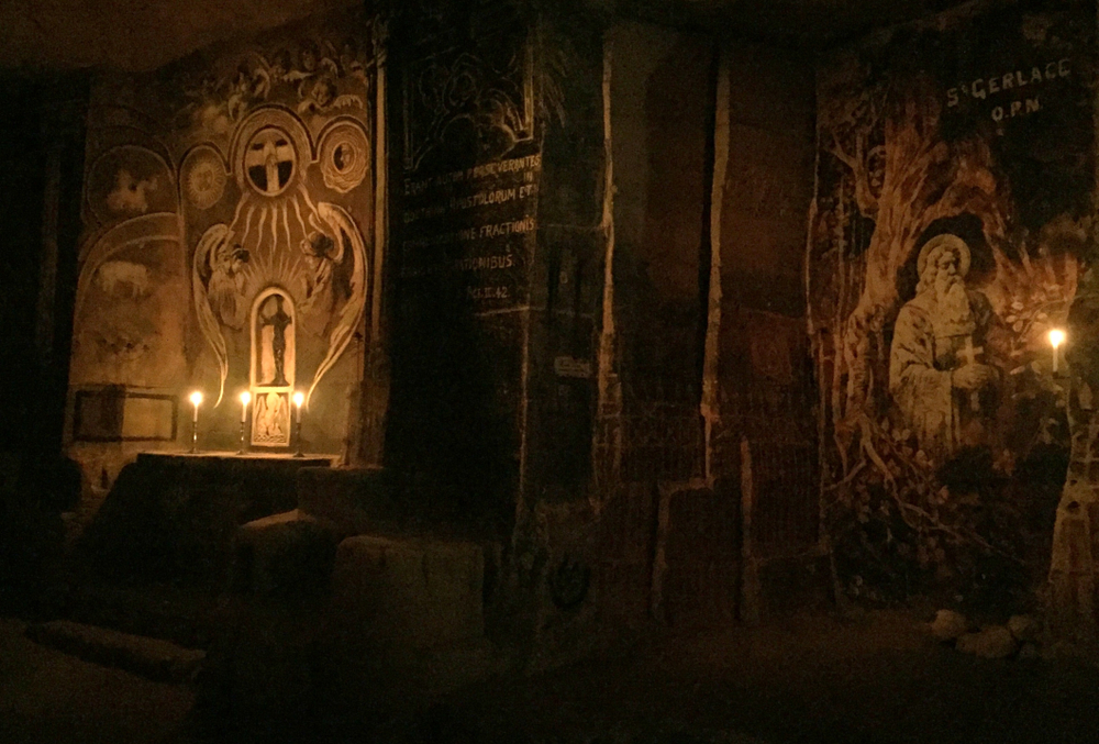 Duas pinturas religiosas em uma caverna, iluminadas à luz de velas